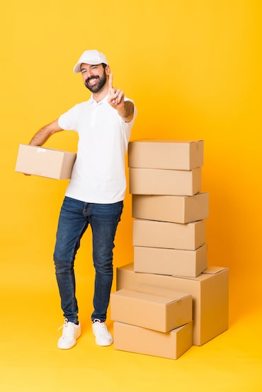 Full-length shot of delivery man among boxes over isolated yellow background showing and lifting a finger